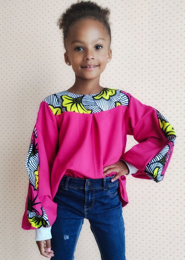 sweat grande taille rose avec des empiècements en wax porté par une fillette face à la camera, elle porte un jean et sourit