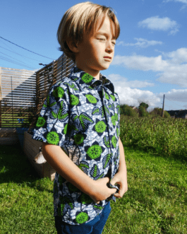 chemise verte en wax à manche courtes portée par un garçon blond tourné de 3/4. Il est debout face au soleil dans la nature et ferme les yeux