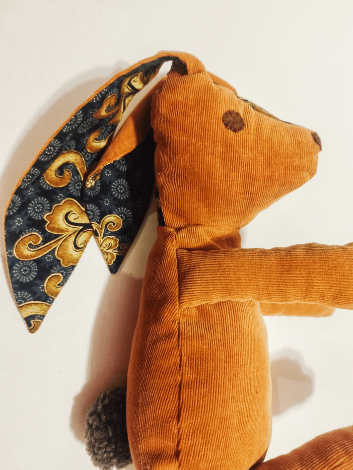peluche de forme animal, il représente un lapin avec des grandes oreilles, la vue est cadré en portrait, la peluche est en velours de couleur citrouille