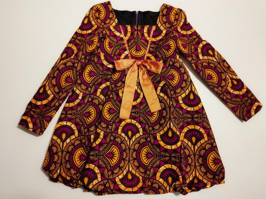 robe en tissu hollandais imprimé, la taille haute est soulignée par un nœud en soie, la robe est bicolore orange et prune