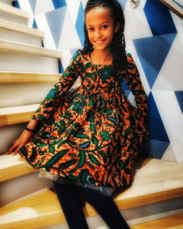 fille assise dans les escalier avec une robe en tissu wax imprimé de feuilles vertes sur fond de couleur brique
