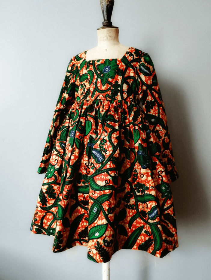 robe en Wax imprimée vert sur fond orange porté par un mannequin de couturière