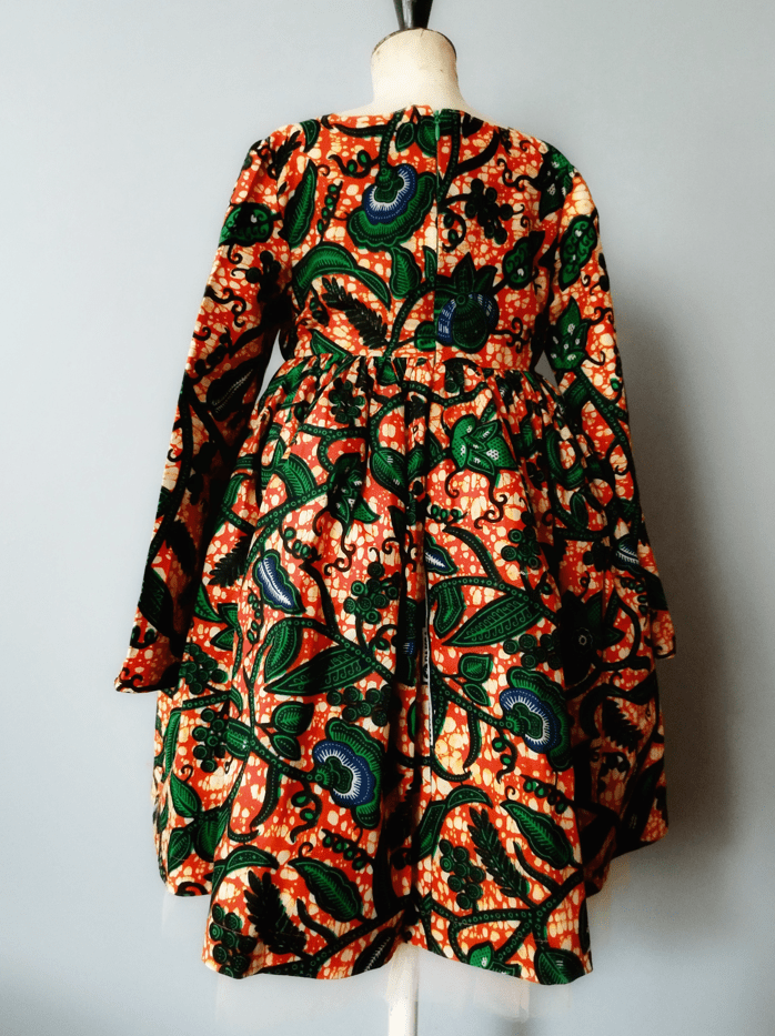 Robe en wax imprimé vert sur fond orange, vue de dos sur un mannequin de bois