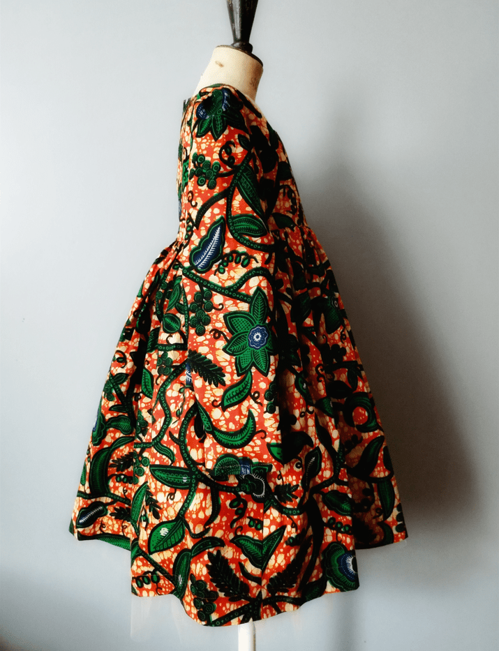 Robe en tissu wax imprimé représentant des feuilles sur un fond orange, sur un mannequin de bois, vue de profil