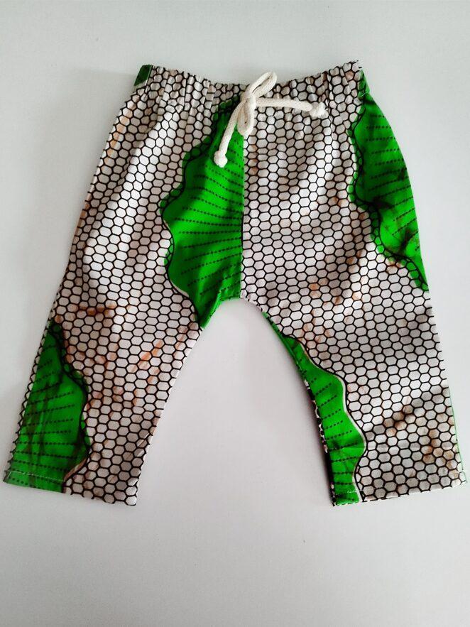 pantalon pour bébé en tissu wax imprimé vert sur fond beige posé à plat