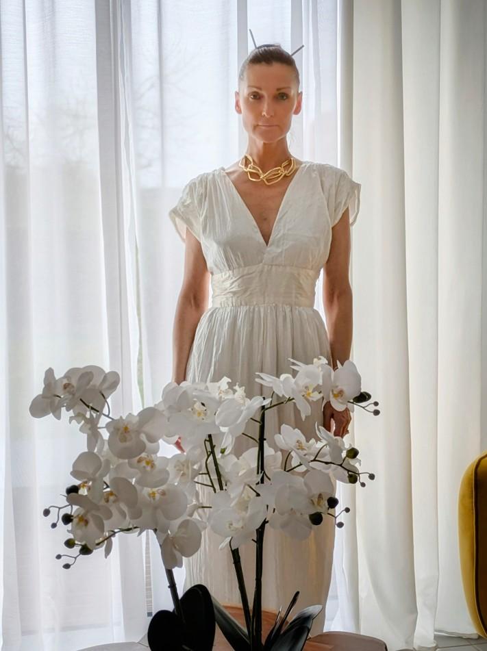 femme derrière un bouquet d'orchidée, porte une robe blanche avec un décolleté en "V"