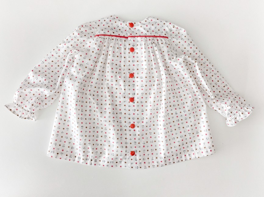 robe pour bébé vue de dos. Il y a des pressions rouges en contraste avec les motifs de la robe