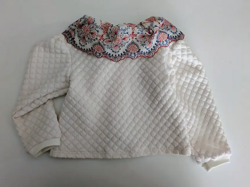 Gilet en maille pour bébé avec un grand col brodé, il est de couleur écru